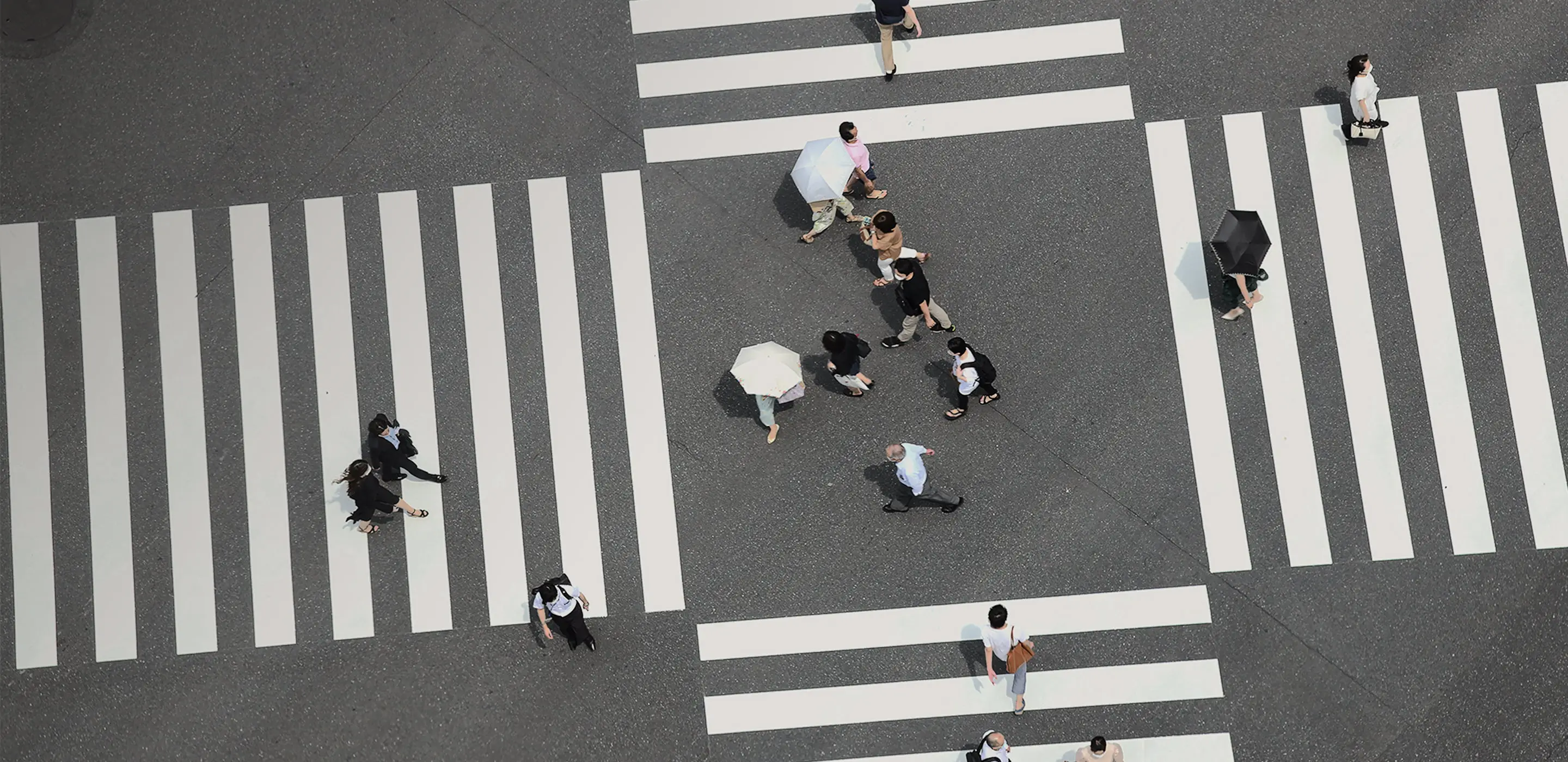 横断歩道を歩く人々を真上から撮影した航空写真。白い日傘を差す人も見える